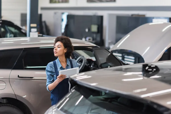 Junger afrikanisch-amerikanischer Mechaniker in Overalls arbeitet mit digitalem Tablet in der Garage — Stockfoto