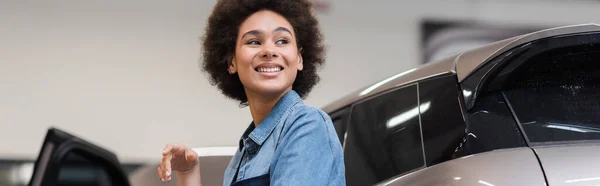 Lächelnder junger afrikanisch-amerikanischer Mechaniker steht mit nahem Auto im Autoreparaturservice, Banner — Stockfoto