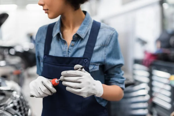 Vista parcial del joven mecánico afroamericano de pie con destornillador en servicio de reparación de automóviles - foto de stock