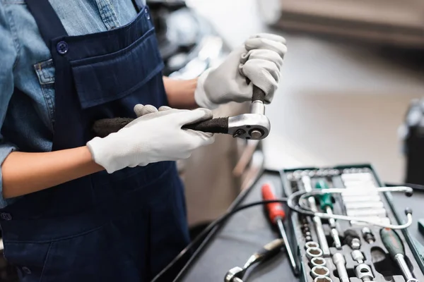 Vista de perto de mãos mecânicas em luvas segurando equipamento de reparação perto caixa de ferramentas na garagem — Fotografia de Stock