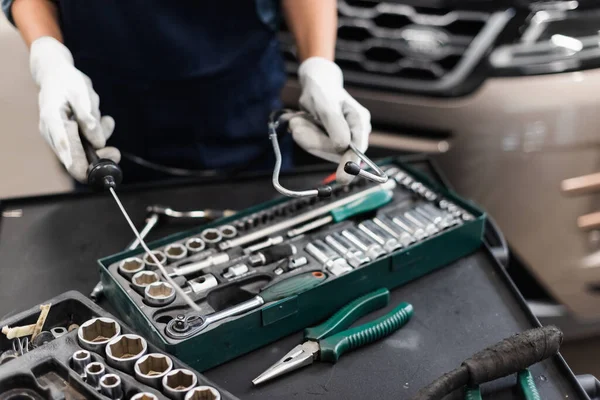 Close up view of mechanic hands in gloves holding diagnostic equipment near toolbox in garage — Stock Photo