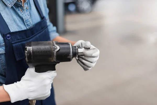 Close up view of mechanic hands in gloves holding electric screwdriver and attachment in garage — Stock Photo