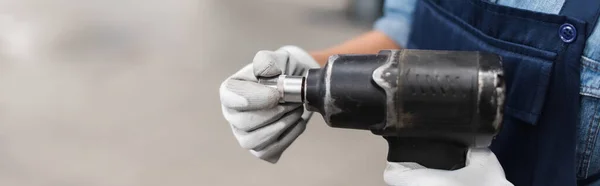 Vista ravvicinata di mani meccaniche in guanti con avvitatore elettrico e attacco su sfondo sfocato, banner — Foto stock