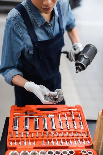 Vista parziale di giovane meccanico con le mani in guanti che tengono cacciavite elettrico vicino cassetta degli attrezzi in servizio di riparazione auto — Foto stock