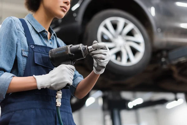 Vista parziale di giovane meccanico con le mani in guanti che tengono avvitatore elettrico nel servizio di riparazione auto — Foto stock