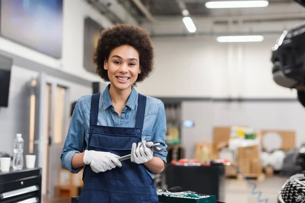 Smiling young african american mechanic holding wrench in auto repair service — Stock Photo