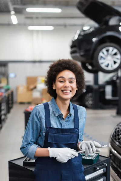 Lächelnder junger afrikanisch-amerikanischer Mechaniker hält Schraubenschlüssel in Garage — Stockfoto