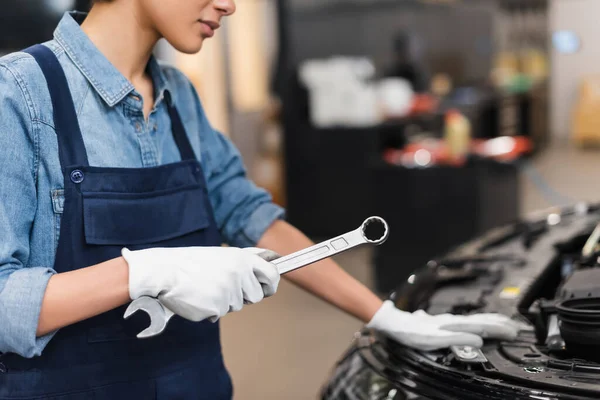 Partial view of young african american mechanic holding wrench near car hood in garage — Stock Photo