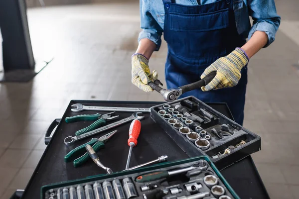 Vista parcial del joven mecánico con las manos en guantes sosteniendo la llave inglesa cerca de las cajas de herramientas en el garaje - foto de stock