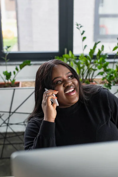 Felice afro americano plus size donna d'affari che parla su smartphone in ufficio — Foto stock