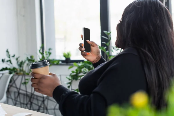 Africano americano plus tamanho empresária olhando para smartphone com tela em branco enquanto segurando copo de papel — Stock Photo
