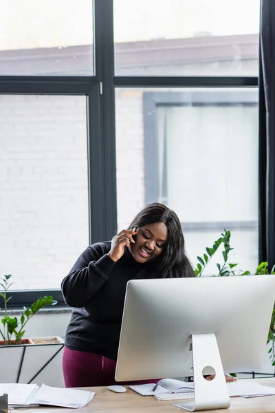 Sorridente afro-americano plus size empresária falando no smartphone no escritório — Fotografia de Stock