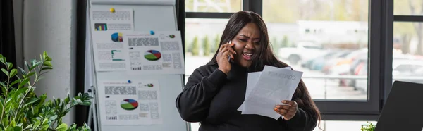 Cheerful african american plus size businesswoman talking on smartphone and holding documents, banner — Stock Photo