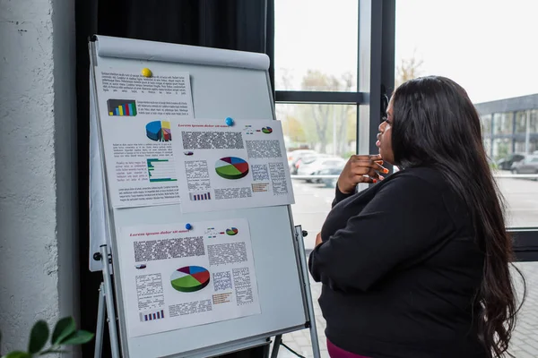 Afro-américaine plus taille femme d'affaires regardant flip chart avec des graphiques et des graphiques — Photo de stock