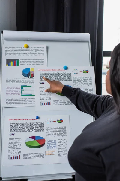 Mujer de negocios afroamericana de tamaño grande señalando el rotafolio con gráficos y gráficos - foto de stock