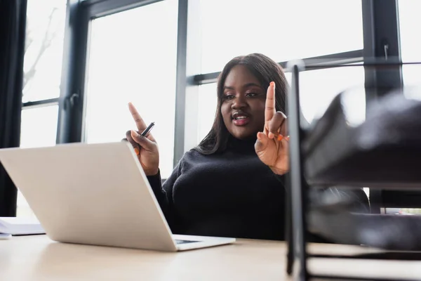 Africano americano más tamaño mujer de negocios gesto mientras que tiene videollamada en el ordenador portátil en la oficina - foto de stock