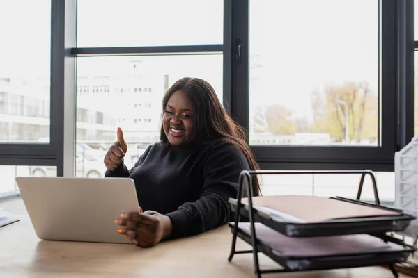 Feliz Africano americano plus tamanho empresária mostrando polegar para cima ao ter chamada de vídeo no laptop no escritório — Fotografia de Stock