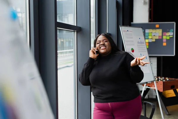 Lächelnde afrikanisch-amerikanische Plus-Size-Frau spricht im Büro auf Smartphone — Stockfoto