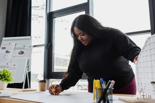 Africano americano más tamaño ingeniero dibujo plano cerca de casa modelo - foto de stock