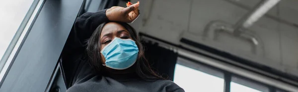 Visão de baixo ângulo de Africano americano plus tamanho empresária em máscara médica sentindo mal no escritório, banner — Fotografia de Stock