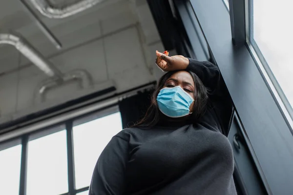 Low angle view of african american plus size businesswoman in medical mask feeling unwell in office — Stock Photo