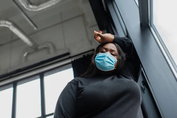 Vista basso angolo di afro americano plus size donna d'affari in maschera medica sensazione di malessere in ufficio — Foto stock