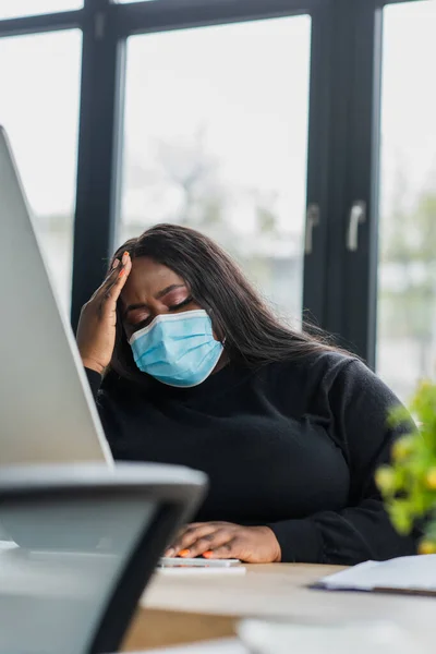 Afro-américaine plus taille femme d'affaires dans le masque médical souffrant de maux de tête — Photo de stock