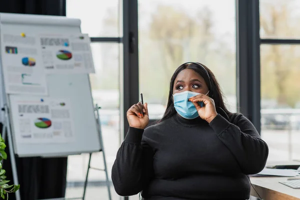 African american plus size operator in headset and medical mask talking in microphone in modern office — Stock Photo