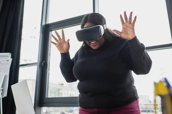 Exited african american plus size woman in vr headset gesturing near laptop — Stock Photo