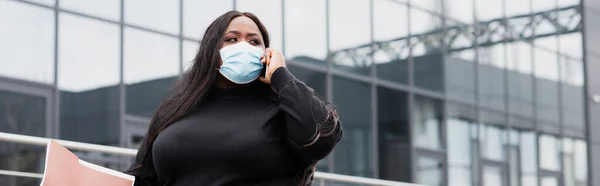 Africano americano más tamaño mujer en médico máscara celebración carpeta y hablar en el teléfono inteligente fuera, pancarta - foto de stock