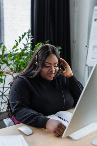 Morena africana americana plus size mulher no fone de ouvido com microfone no escritório — Fotografia de Stock