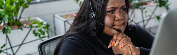 Cher opérateur afro-américain plus taille dans casque avec microphone regardant moniteur d'ordinateur, bannière — Photo de stock