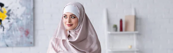 Mujer árabe bonita en hijab mirando hacia otro lado en casa, pancarta - foto de stock