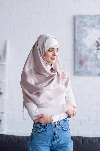 Mujer musulmana positiva de pie con los brazos cruzados en casa - foto de stock