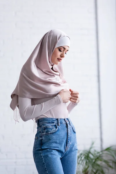 Timida donna musulmana toccare hijab mentre in piedi a casa — Foto stock