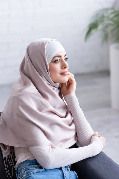 Mujer musulmana soñadora sonriendo mientras mira a casa - foto de stock