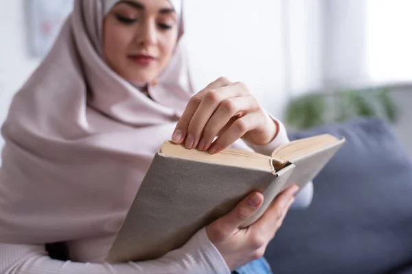 Mujer musulmana borrosa leyendo novela en casa - foto de stock