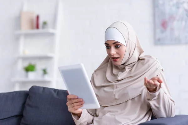 Entmutigte Muslimin gestikuliert, während sie zu Hause auf dem Sofa ein digitales Tablet benutzt — Stockfoto