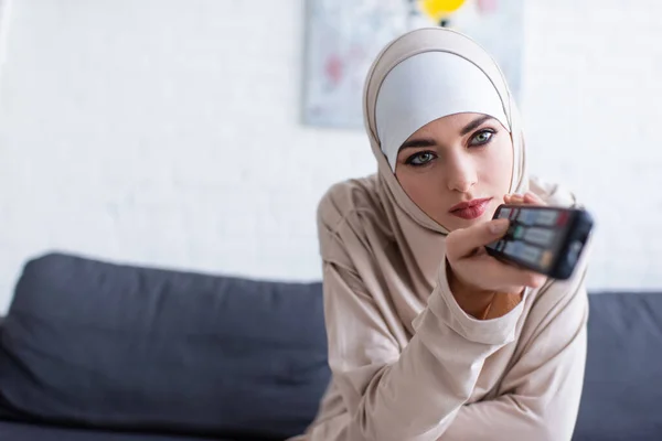 Giovane donna araba in hijab cliccando canali mentre guardando la tv a casa — Foto stock