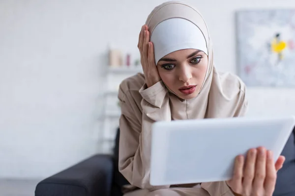 Femme musulmane choquée toucher la tête tout en regardant tablette numérique à la maison — Photo de stock