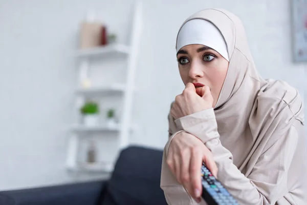 Femme arabe nerveuse tenant la main près du visage tout en regardant la télévision à la maison — Photo de stock