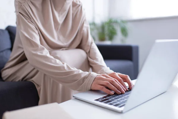 Vista cortada de mulher muçulmana digitando no laptop em primeiro plano desfocado — Fotografia de Stock