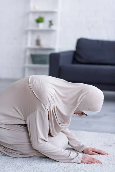 Muslim woman in hijab and abaya praying on carpet at home — Stock Photo