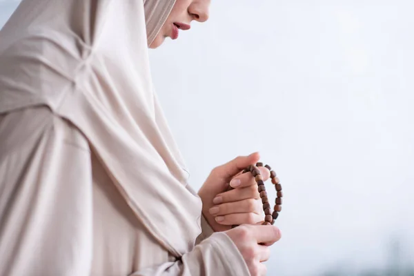 Частичный взгляд молодой арабской женщины, держащей четки во время молитвы на дому — стоковое фото
