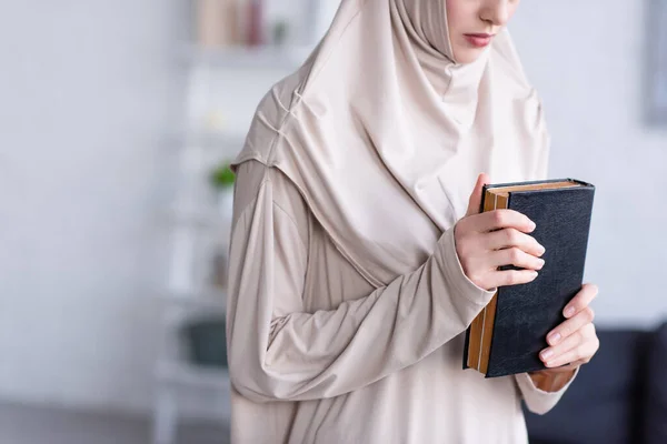 Visão parcial da mulher árabe no hijab segurando Corão enquanto reza em casa — Fotografia de Stock