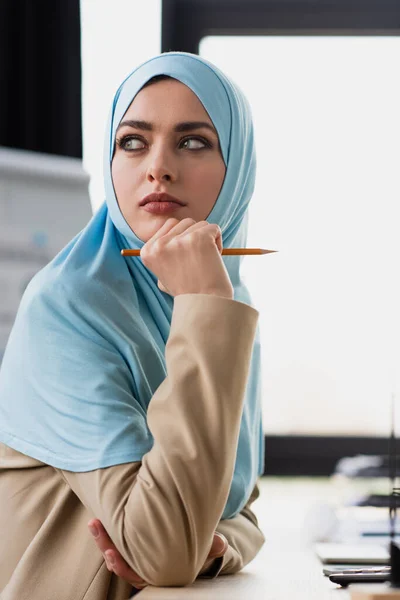 Ingénieur musulman réfléchi tenant stylo tout en regardant loin dans le bureau — Photo de stock