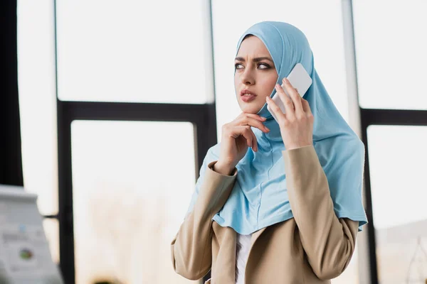 Thoughtful arabian businesswoman in hijab talking on cellphone in office — Stock Photo