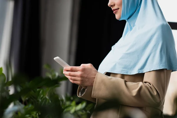 Cropped view of arabian businesswoman in hijab chatting on cellphone in office — Stock Photo