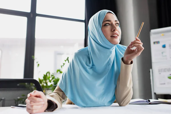Позитивный мусульманский инженер держит ручку, думая в офисе — стоковое фото