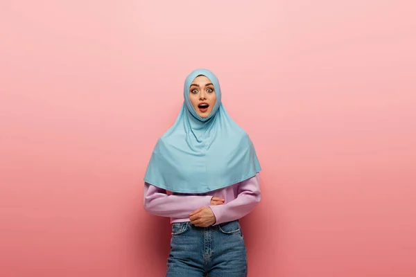 Erstaunt arabische Frau in Hijab und Jeans schaut in die Kamera auf rosa Hintergrund — Stockfoto